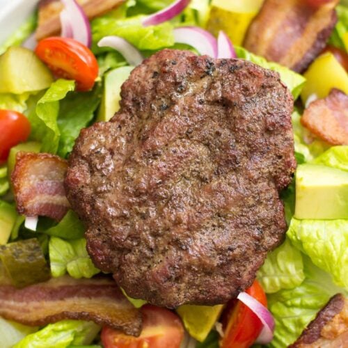 A burger salad with dill pickle vinaigrette in a white bowl