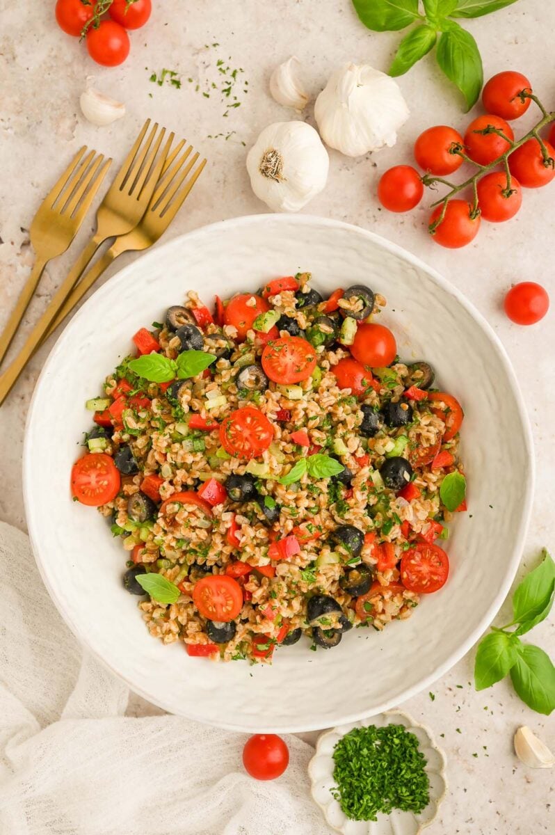 Easy Farro Salad in a white bowl with tomatoes and fresh herbs on the side.