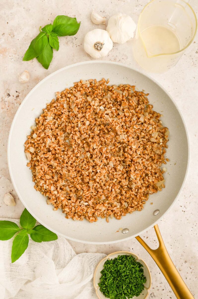 Toasted farro in a pan with fresh basil and garlic on the side.