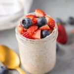 berry overnight oats in a mason jar with a gold spoon on the side on a grey background