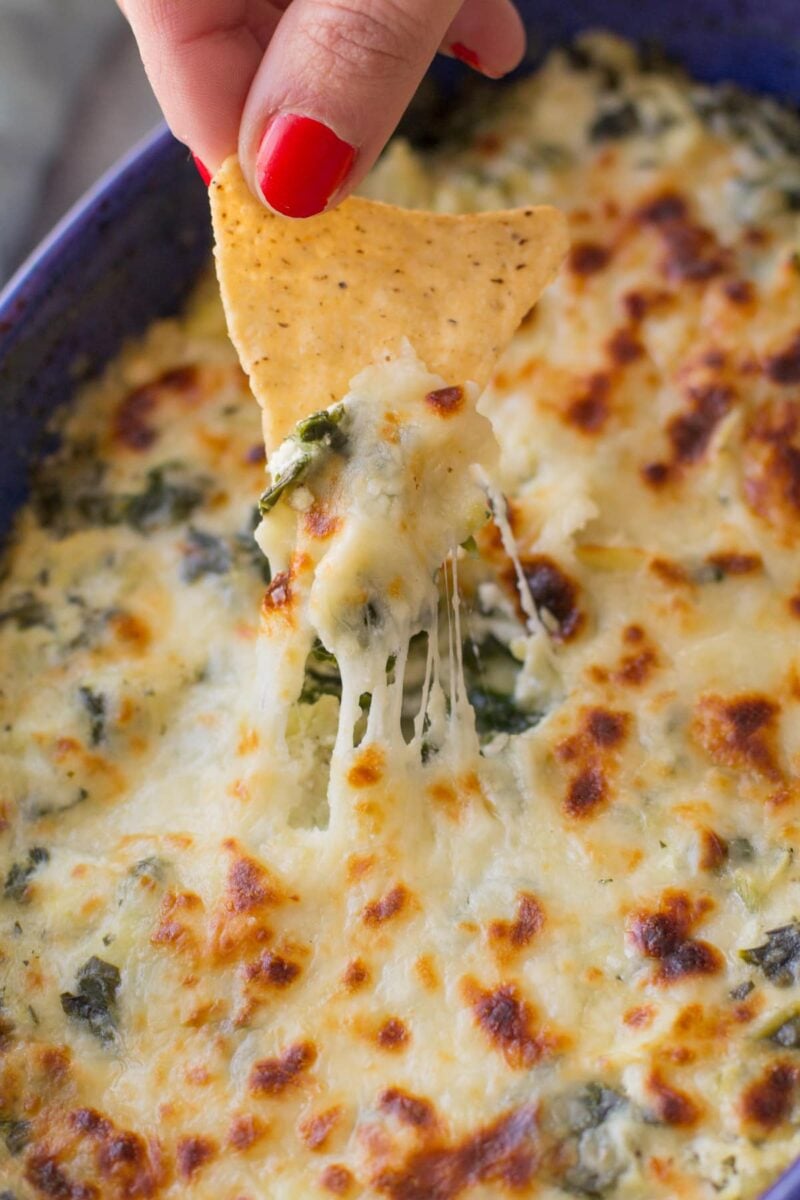 a chip scooping into Healthy Spinach Artichoke Dip, the dip is warm, melty and cheesy