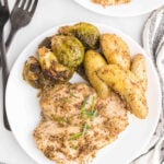 maple mustard chicken on a white plate with brussels sprouts and potatoes on a grey background