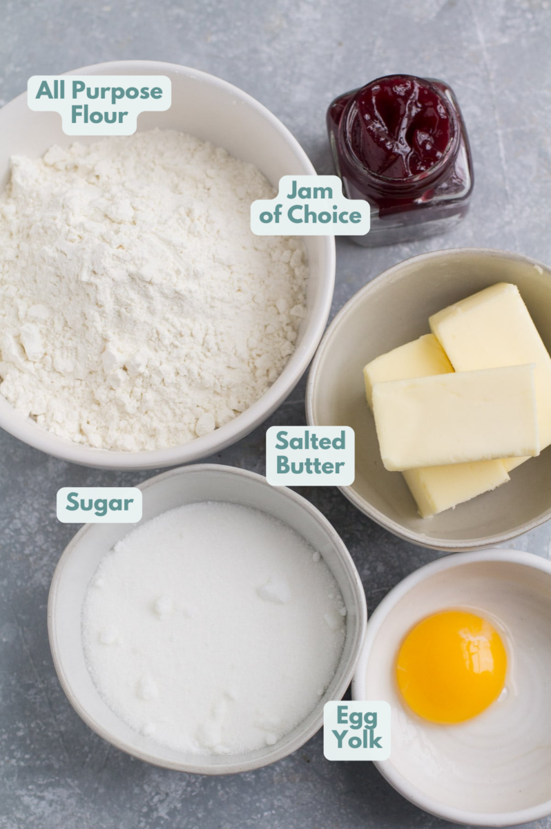 Ingredients of Thumbprint Cookies in small white bowls: egg yolk, sugar, butter, flour and jam