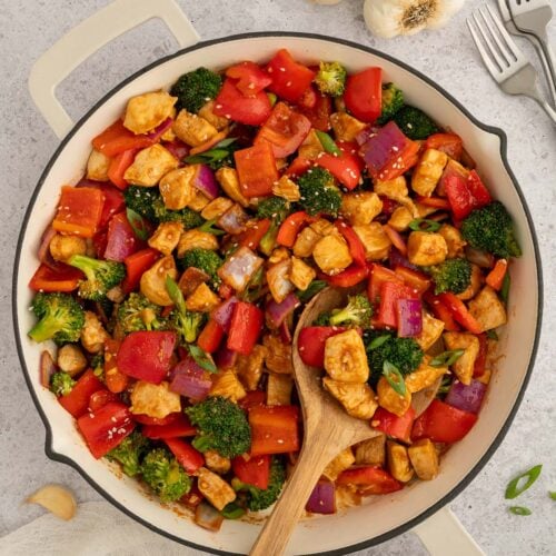 Healthy Sweet & Sour Chicken in a skillet with a wooden spoon in it.