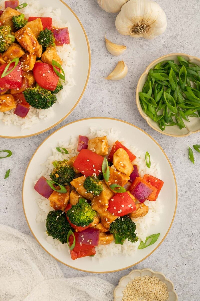 Healthy Sweet and Sour Chicken over white rice on a plate with another plate and bowl of green onions on the side.