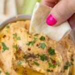 The best authentic hummus recipe with a piece of pita taking a scoop out of it