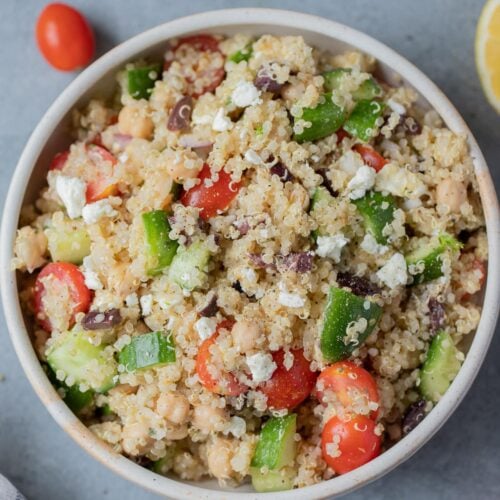 A bowl of Mediterranean Quinoa Salad on a grey background with tomatoes off to the side.