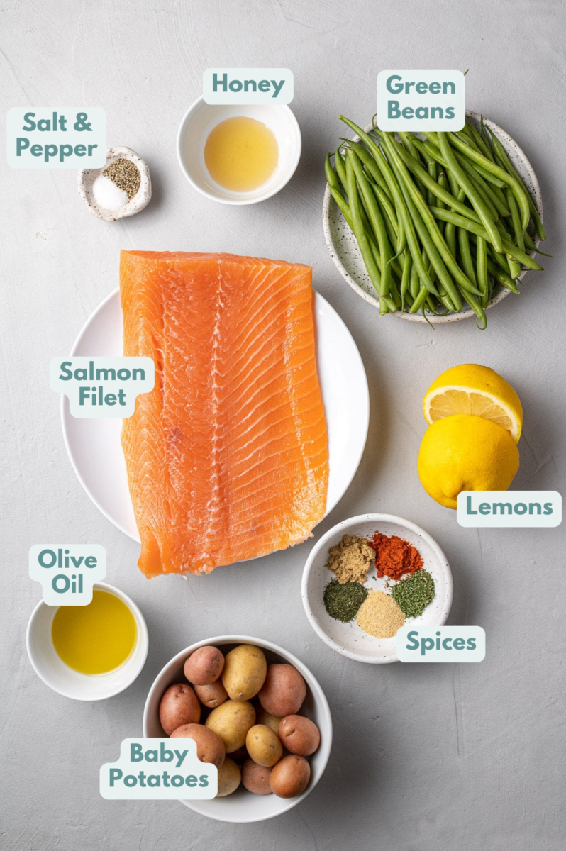 Lemon Salmon Ingredients in small white bowls on a grey background: olive oil, lemon juice, honey, spices, salmon fillet, baby potatoes, green beans
