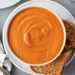 An overhead shot of tomato basil soup with grilled cheese on the side