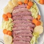 slow cooker corned beef on a white platter surrounded by cabbage, carrots and potatoes
