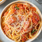 An overhead shot of spaghetti sauce with fresh tomatoes over spaghetti noodles and cheese on a grey background
