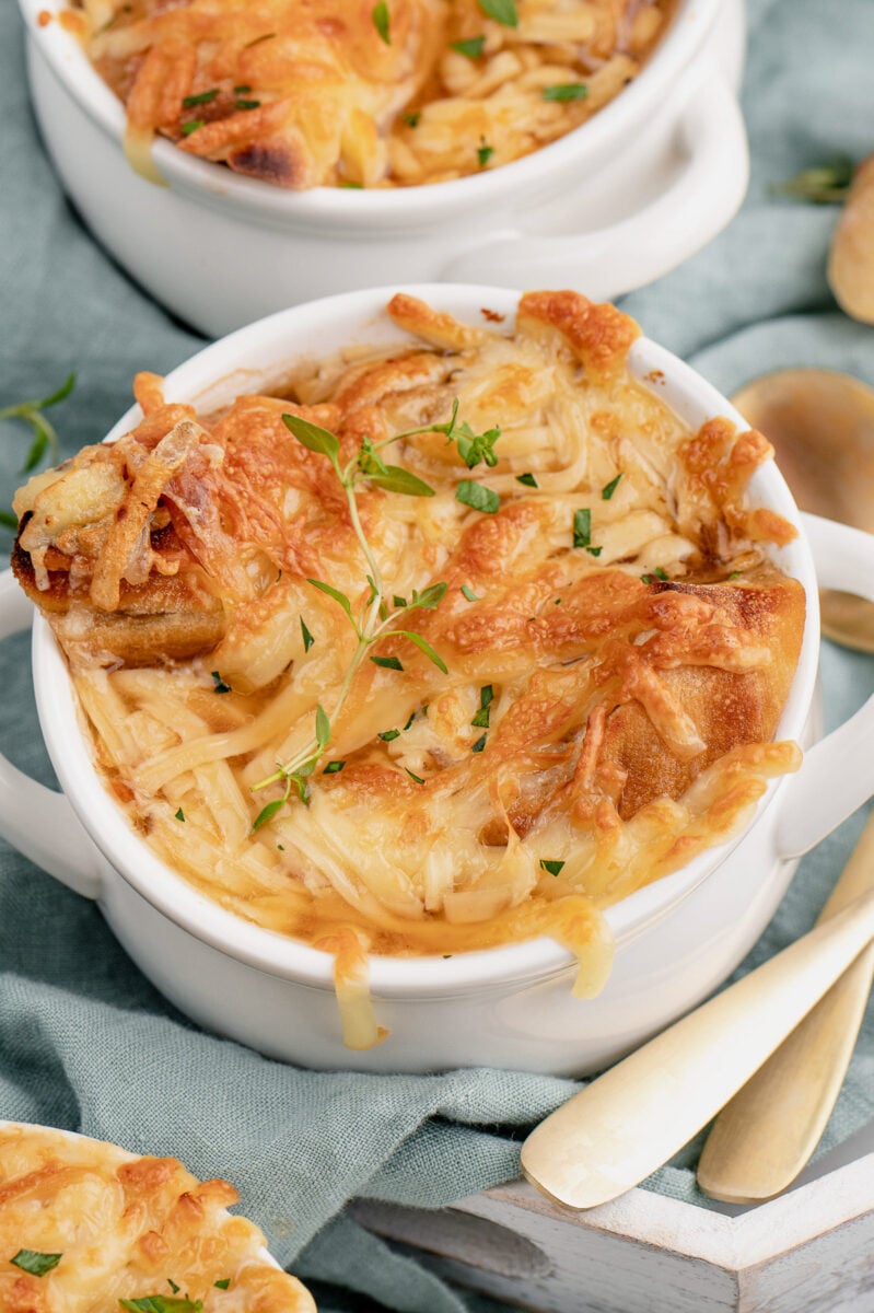 A white bowl of easy french onion soup on a blue towel with another bowl in the background