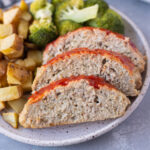 A plate with ground turkey meatloaf sliced beside some broccoli and roasted potatoes on a grey background