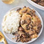 A white plate with Marsala Chicken and white rice with gold forks and a pan of chicken on the side