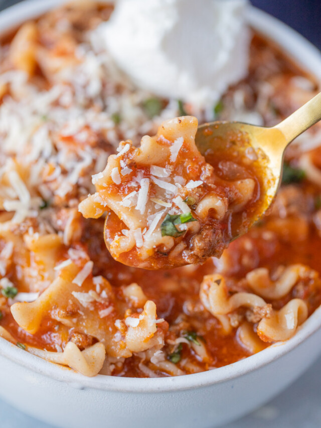 A gold spoon taking a bite out of a bowl of lasagna soup