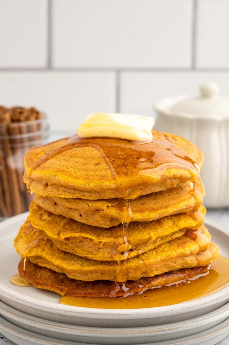 A stack of sweet potato pancakes with a pat of butter and covered in syrup on a white plate on a white background