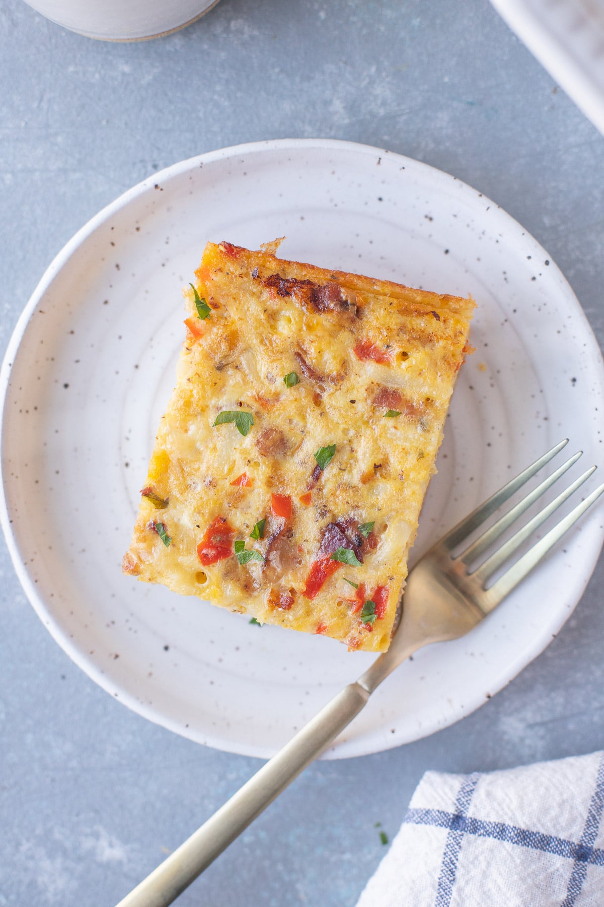 An overhead shot of a piece of bacon breakfast casserole on a white plate with a fork.