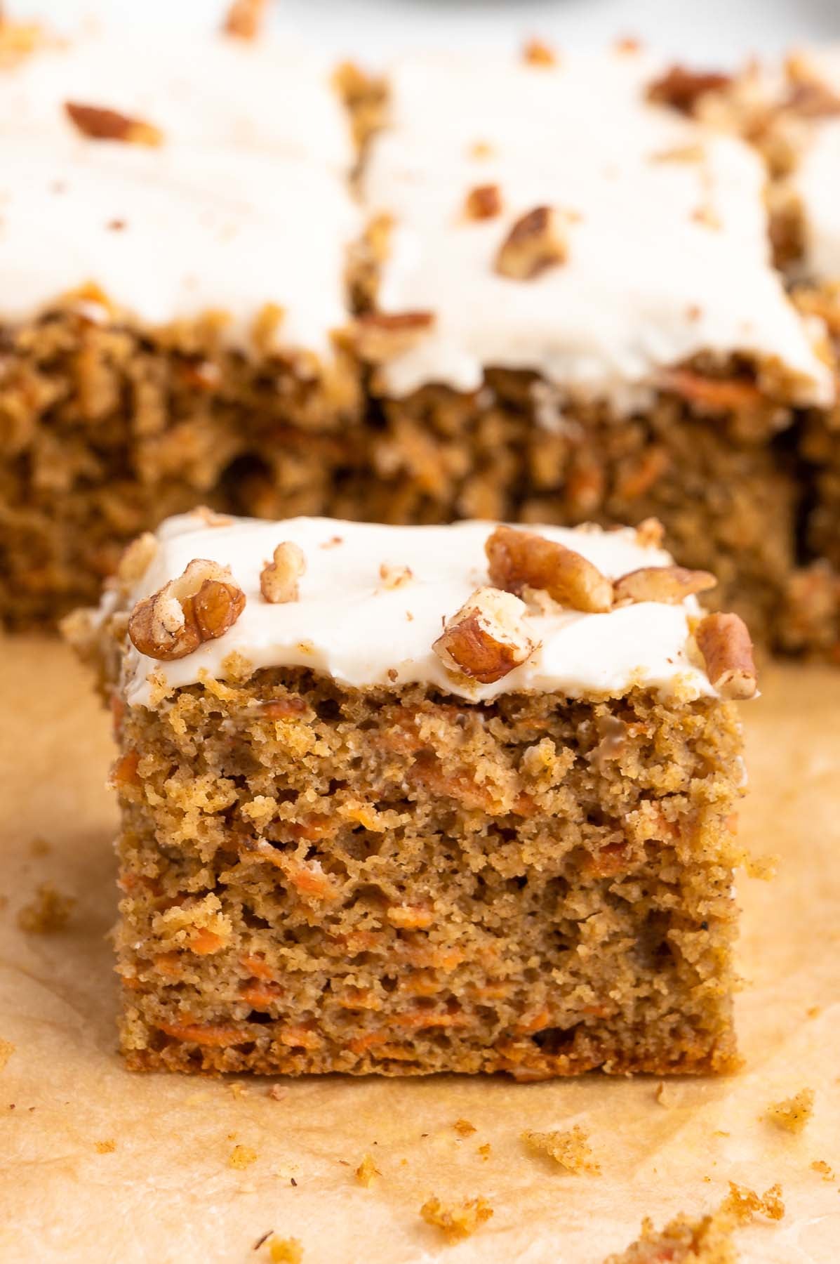Close up, side view of gluten free carrot cake topped with cream cheese frosting and chopped walnuts.