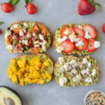 4 pieces of avocado toast (caprese toast, strawberry toast, mango tajin toast, goat cheese toast) on a grey background with tomatoes, basil, strawberries, avocado, and everything bagel seasoning on the side