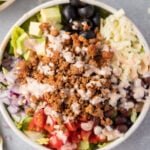 A close up of healthy taco salad in a white bowl topped with a creamy taco dressing