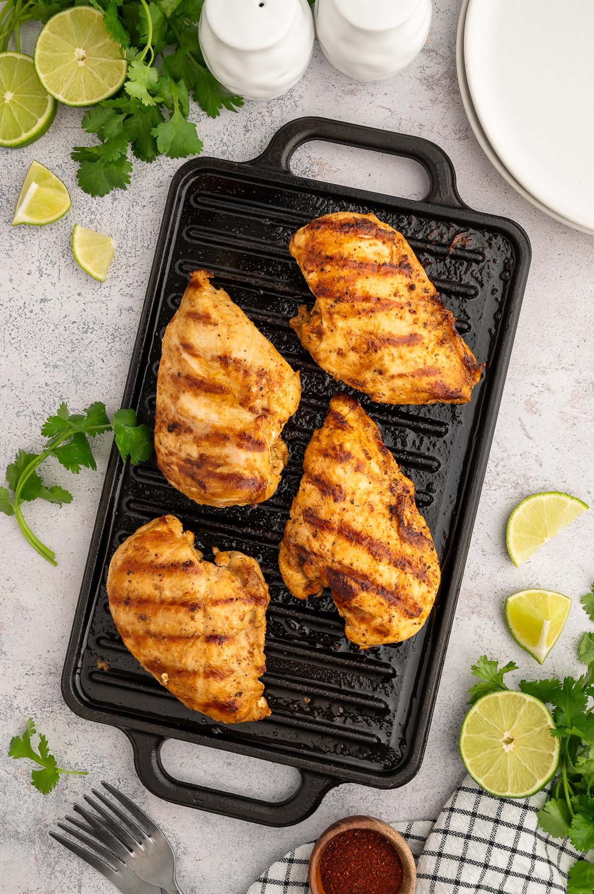 Overhead view of chili lime chicken on a cast iron grill with slices of lime and fresh cilantro on the side.