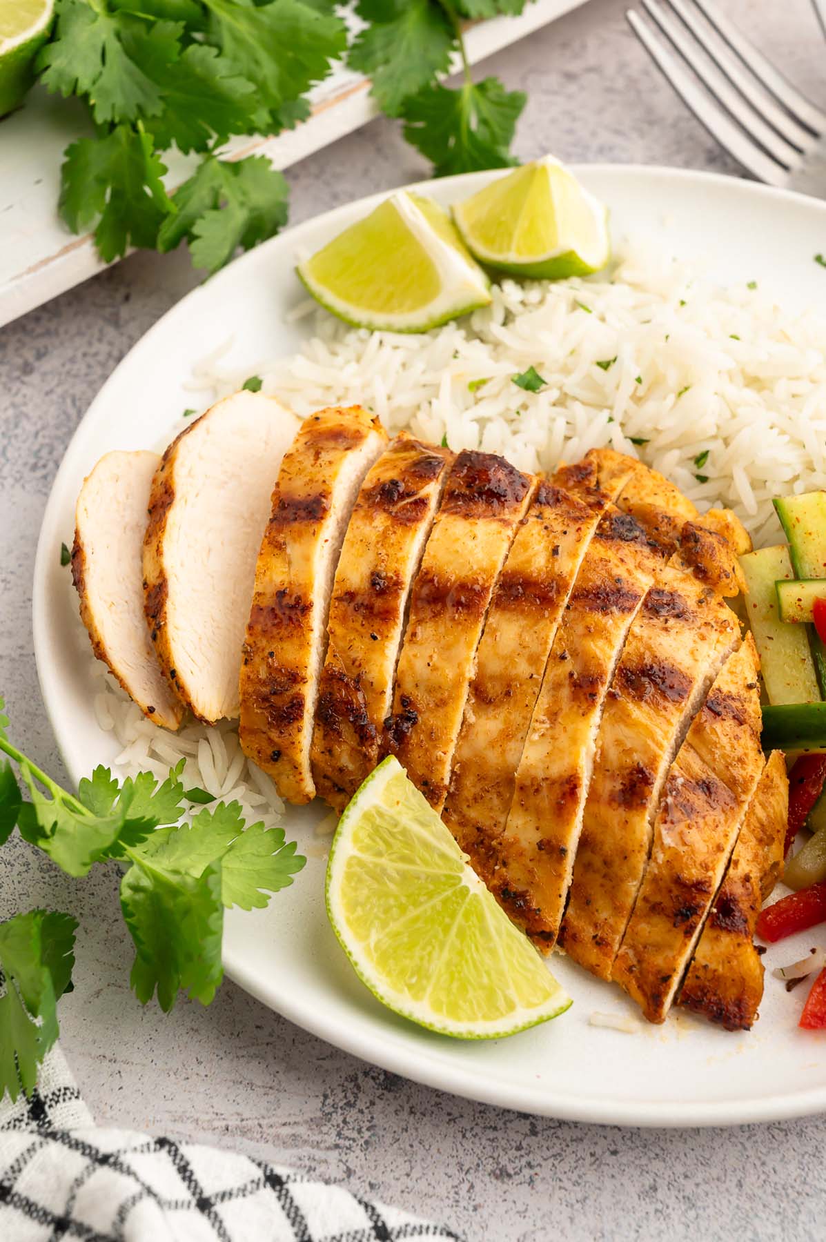 A sliced Chili Lime Chicken Breast on a white plate with cilantro lime rice and pickled veggies on the side.