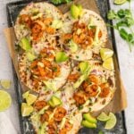 5 Chili Lime Shrimp Tacos on a black sheet pan with chili powder, limes, and cilantro on the side.
