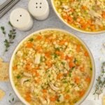 Chicken and Stars Soup in a bowl with another bowl of the soup and spoons on the side.