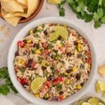 Taco Chicken Salad in a white bowl with bowls of tortilla chips and sliced limes and fresh cilantro on the side.