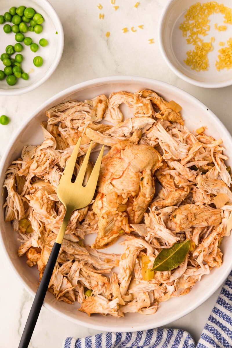 Shredded chicken on a white plate with a fork on top. 