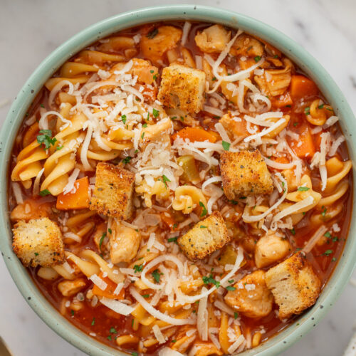 A bowl of chicken parmesan soup topped with croutons on a counter.
