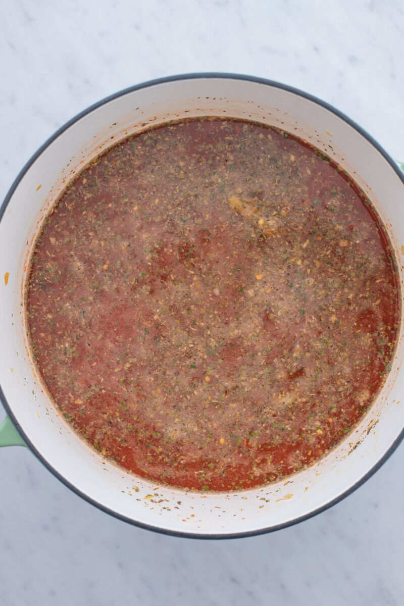 Ingredients for chicken parmesan soup (except for pasta, croutons, and cheese) cooking in a dutch oven.