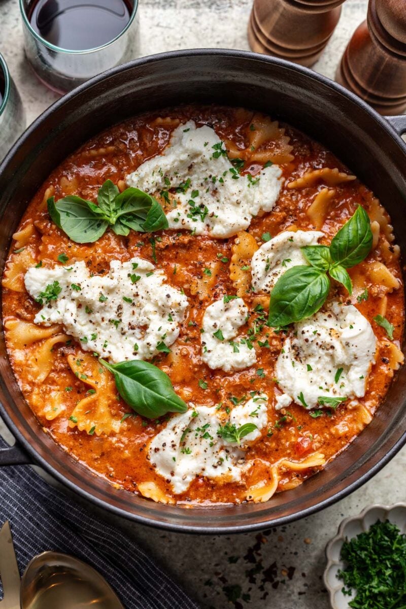 An overhead shot of one pot lasagna in a dutch oven garnished with melty cheese and fresh basil. 