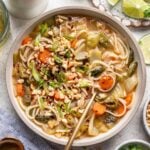 Chicken Rice Noodle Soup in a bowl with a spoon in it with more ingredients on the side.