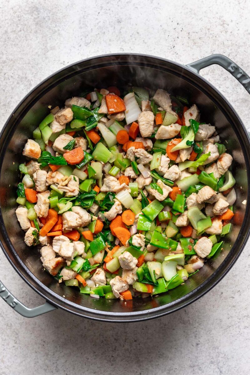 Browned chicken pieces and veggies in a dutch oven. 