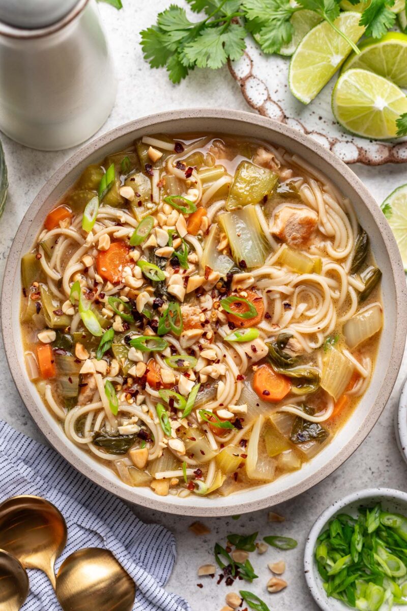 A bowl of chicken rice noodle soup with limes and cilantro on the side.