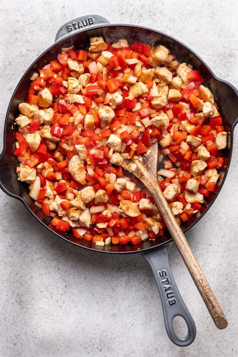Ingredients for healthy cajun chicken in a cast iron skillet with a wooden spoon in it. 