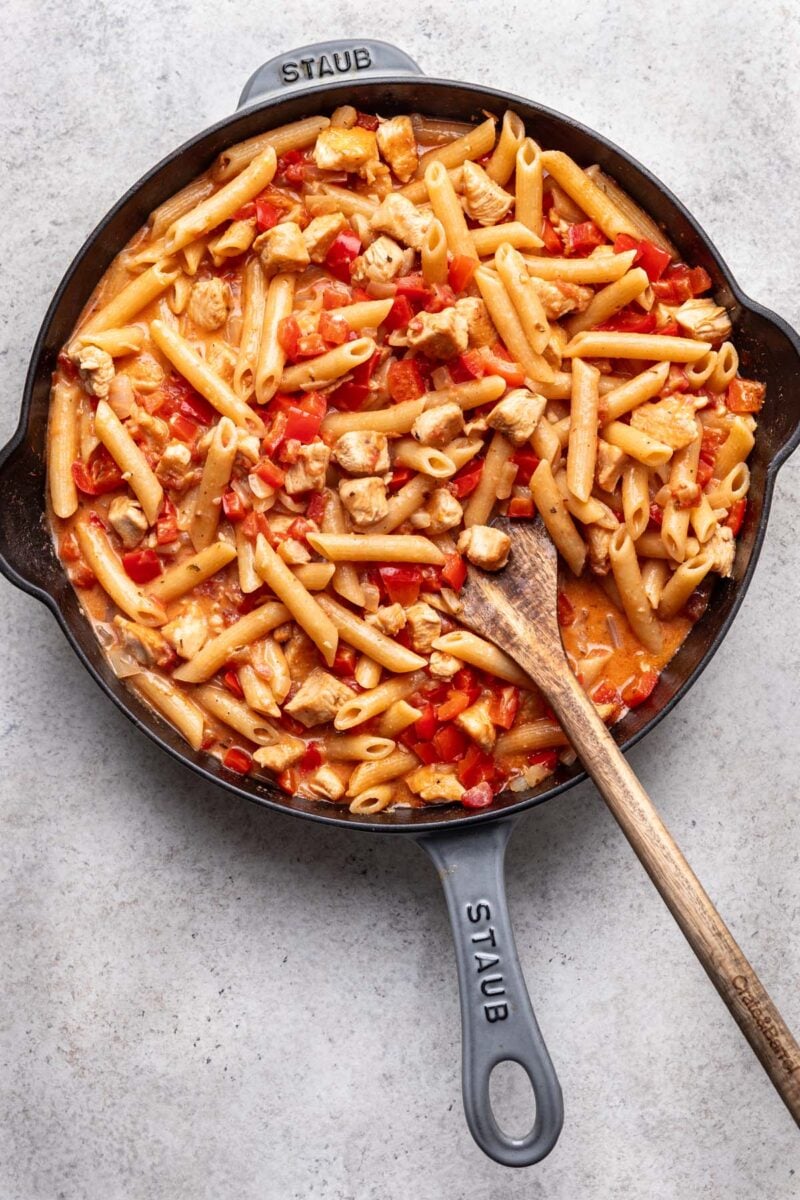Healthy Cajun Chicken Pasta in a cast iron skillet with a wooden spoon in it. 