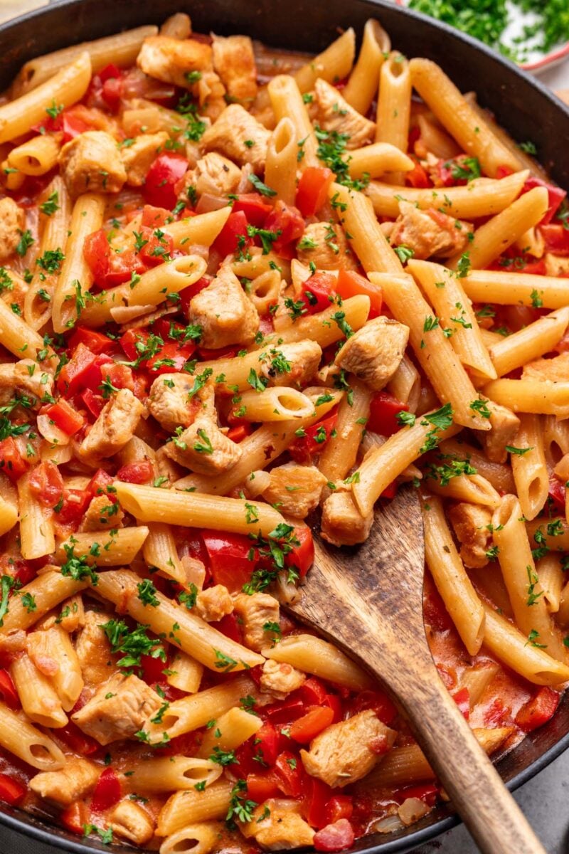 A close up of cajun chicken pasta in a cast iron skillet with a wooden spoon in it. 