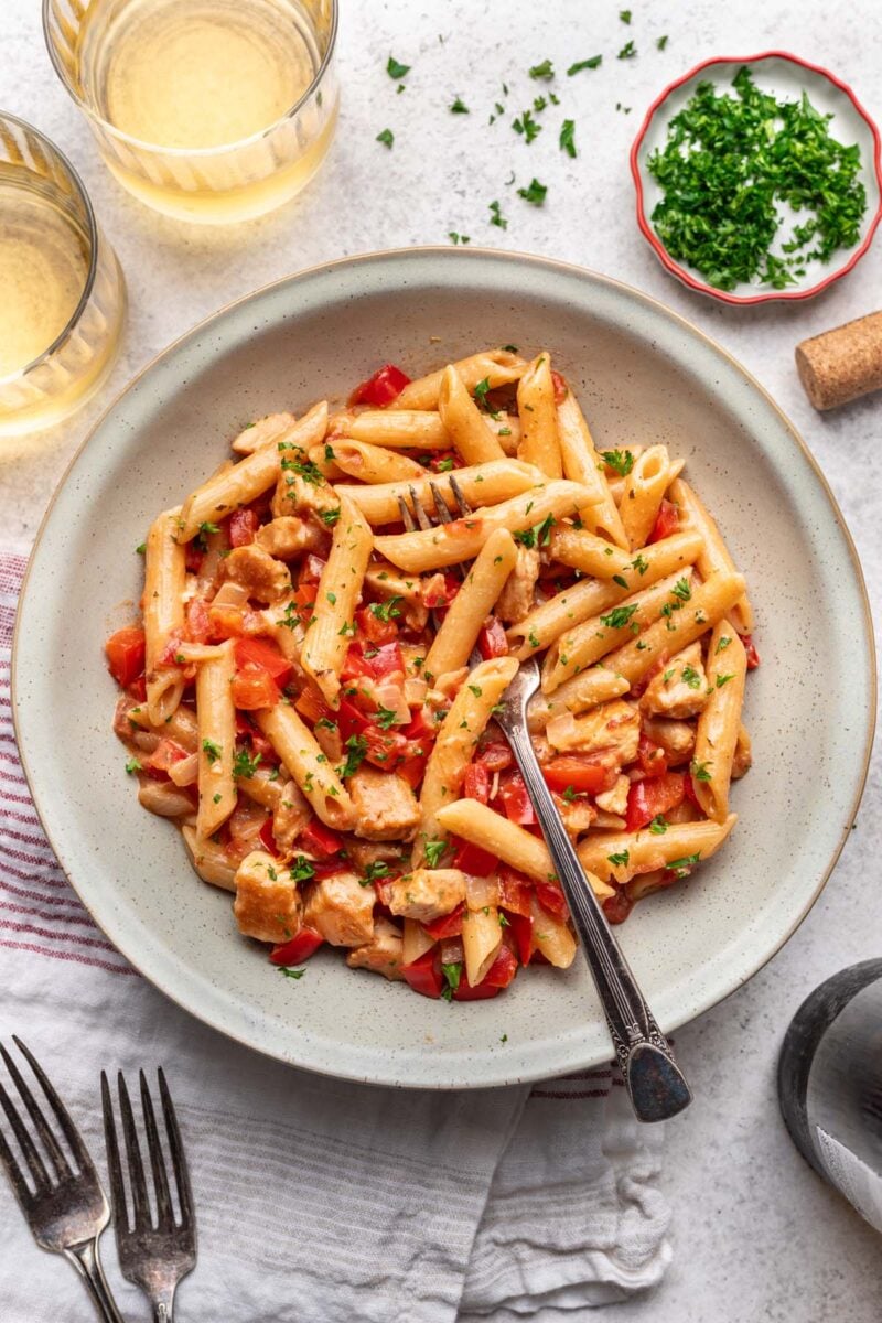 Cajun Chicken Pasta in shallow bowl with a fork in it with two glasses on the side.