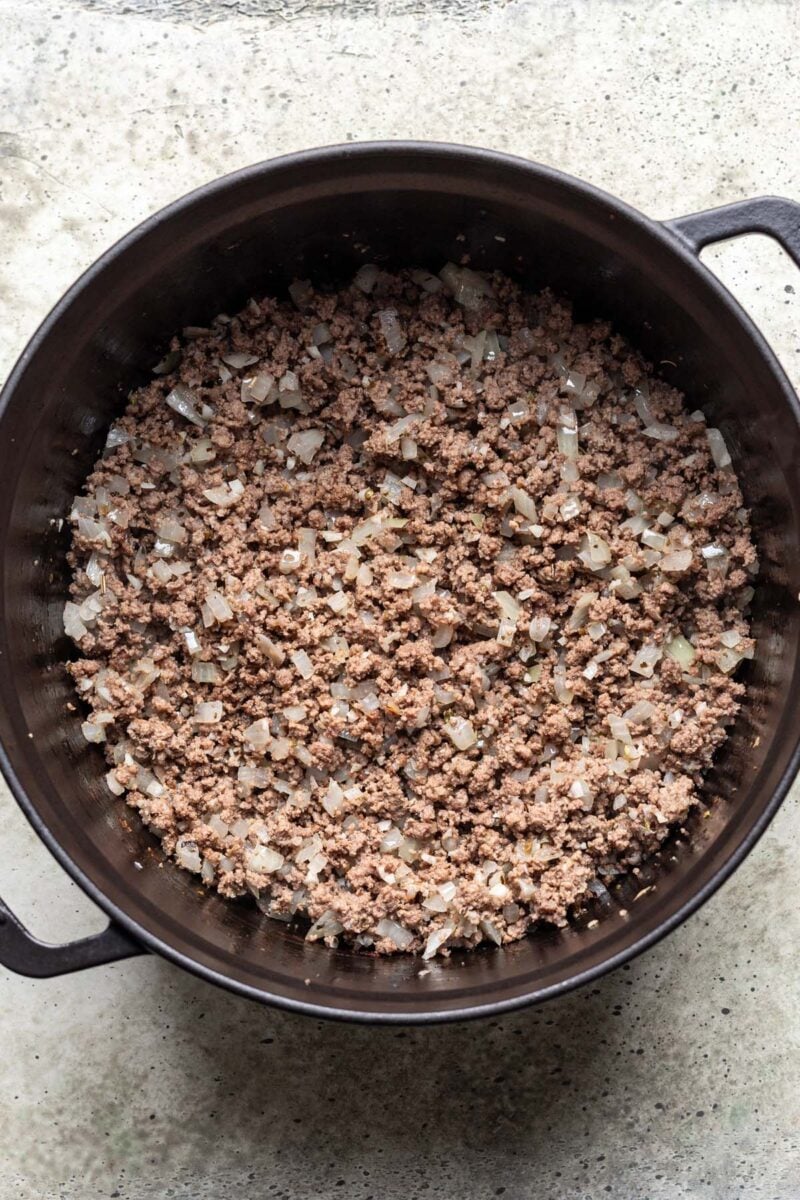 Ground beef, onion, garlic and other ingredients for one pot lasagna in a dutch oven. 
