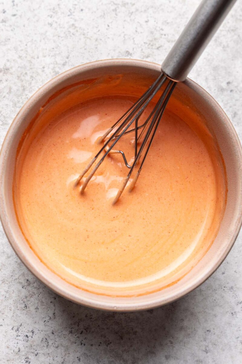 Buffalo greek yogurt sauce in a small bowl with a whisk resting in the sauce.