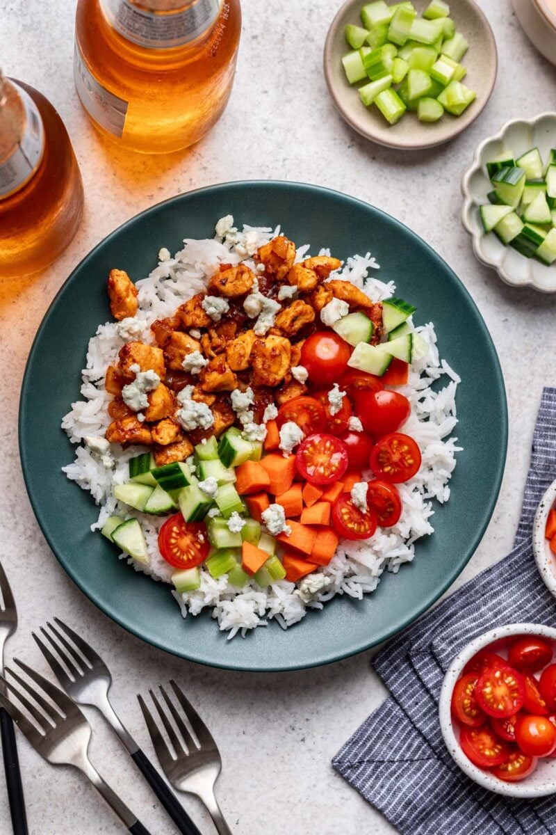 A buffalo chicken bowl (chicken, rice topped with veggies and with buffalo sauce) and bowls of veggies on the side.