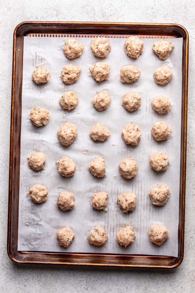 Uncooked little meatballs on a parchment lined baking sheet.