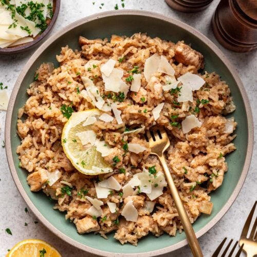 Lemon Parmesan Chicken and Rice on a sage colored plate garnished with a lemon slice and a fork in the rice.