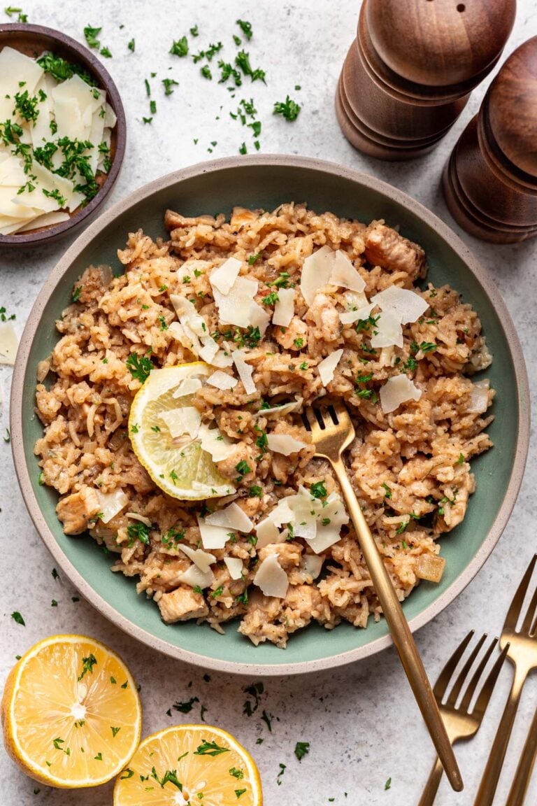 Lemon Parmesan Chicken and Rice on a sage colored plate garnished with a lemon slice and a fork in the rice.