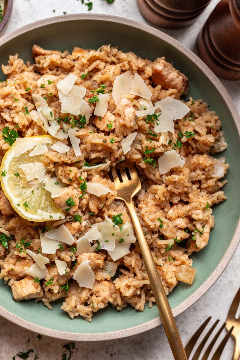 Lemon Parmesan Chicken and Rice on a plate garnished with a lemon slice, parmesan pieces, and herbs and a fork in the rice.