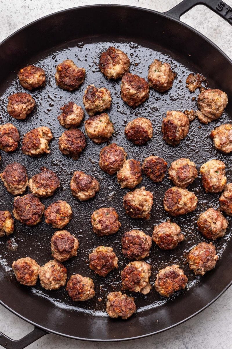 Meatballs cooking in a cast iron skillet. 