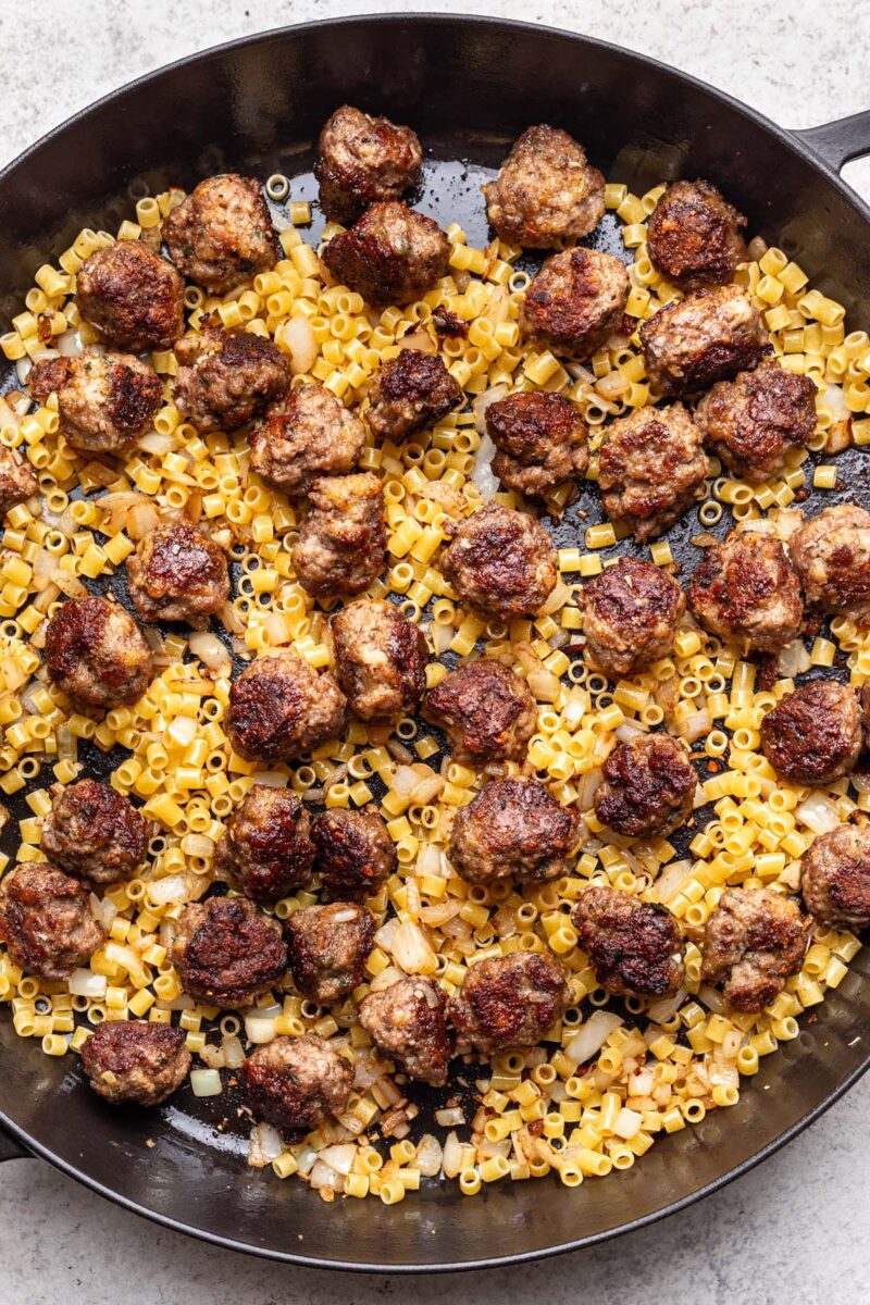 Meatballs, onion, garlic, and pasta in a cast iron skillet. 
