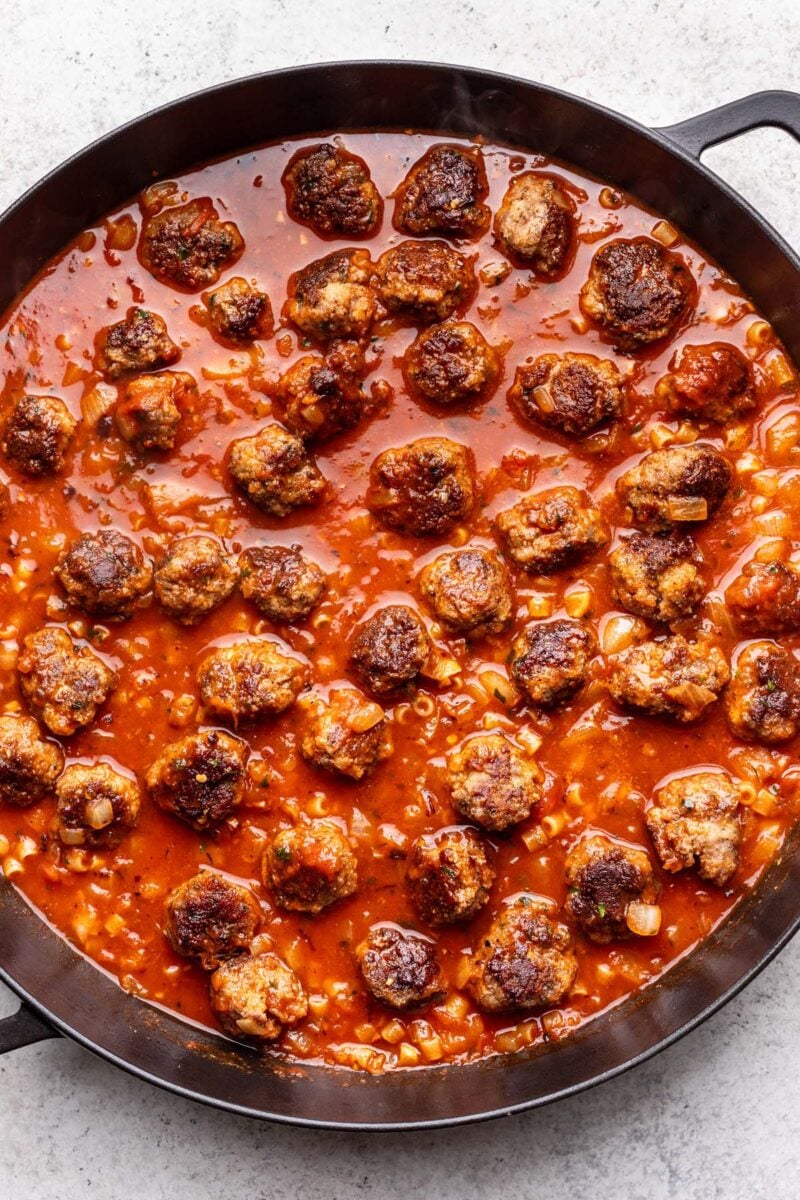 Partially cooked meatball pasta with marinara and broth unabsorbed. 